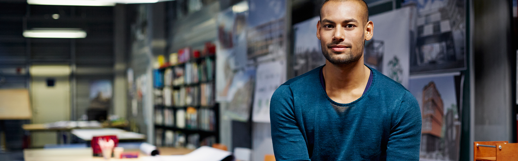  Ung man med blå tröja sitter på ett bord i ett arkitektkontor