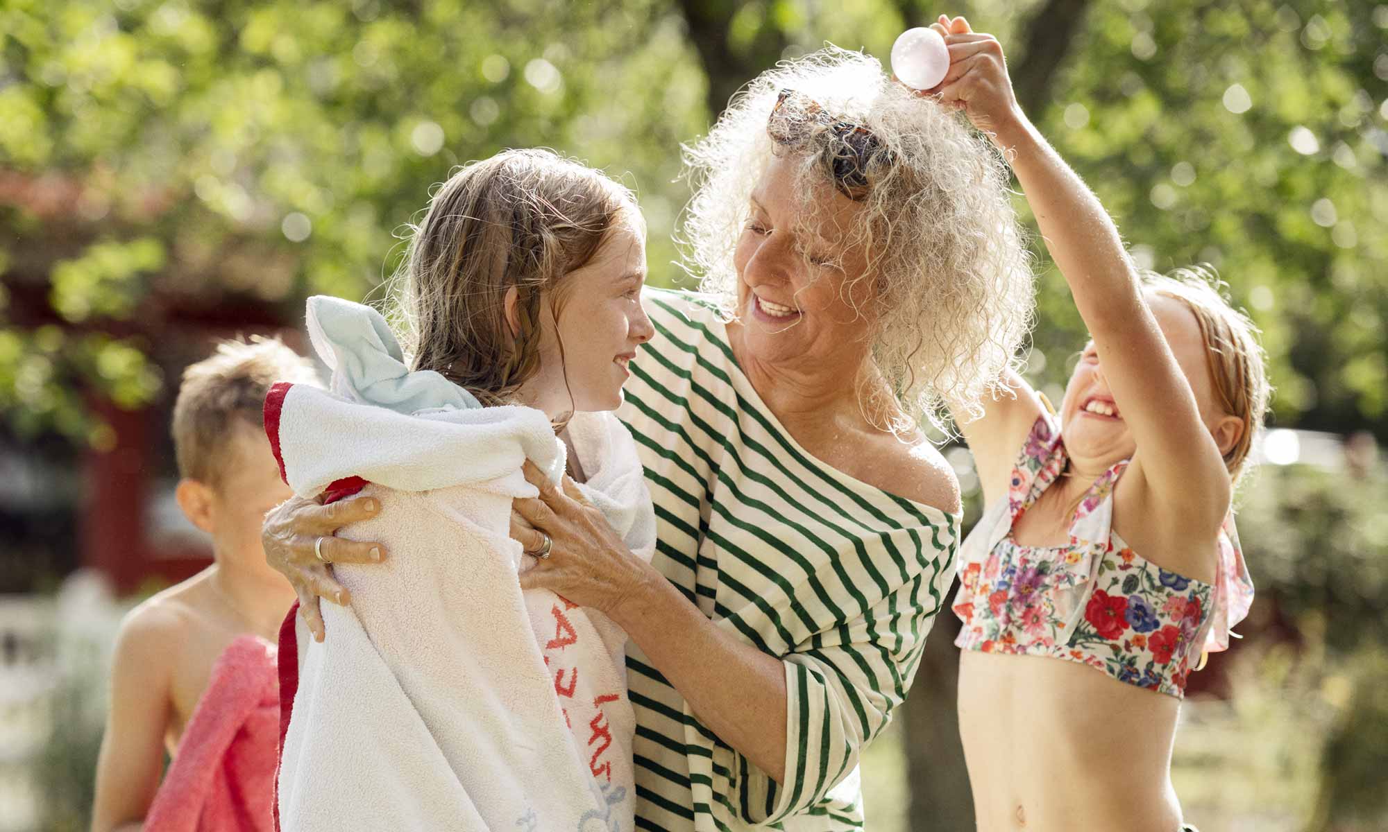 Kvinna står i en trädgård en solig sommardag och torkar barn som har badat