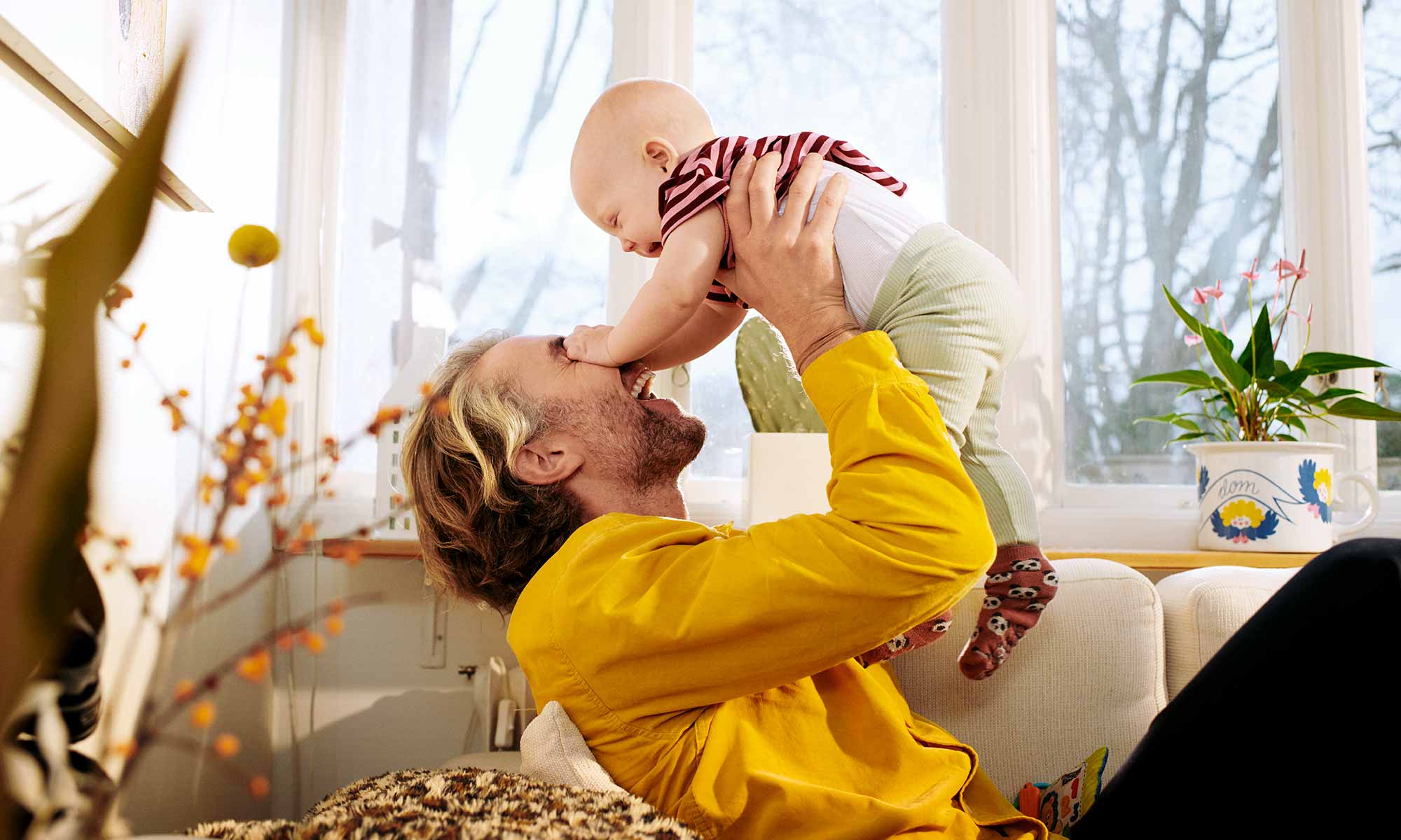 Glad pappa sitter i soffan och leker med sin bebis