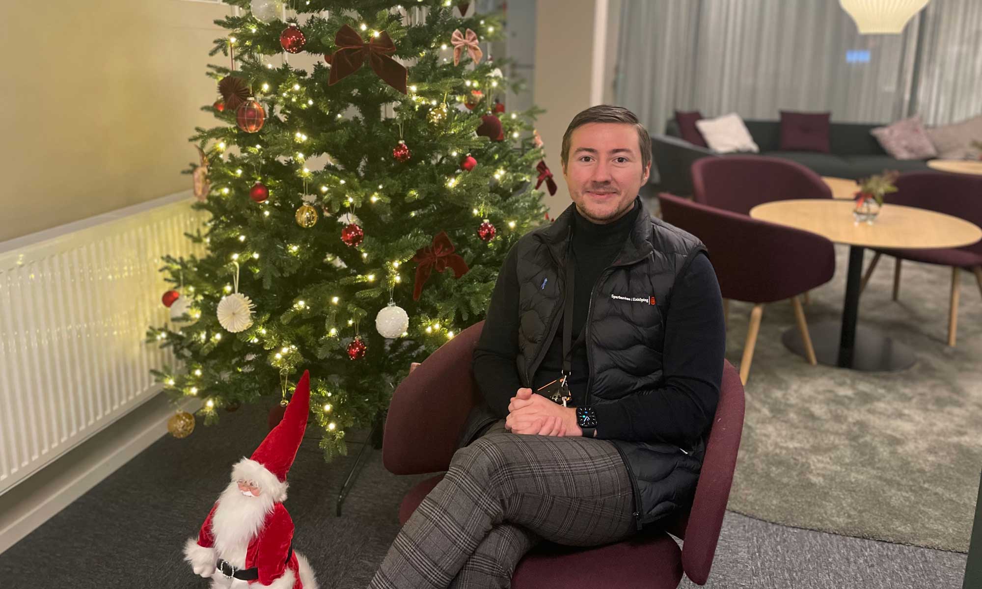 a man dressed in black sitting in front of a christmas tree