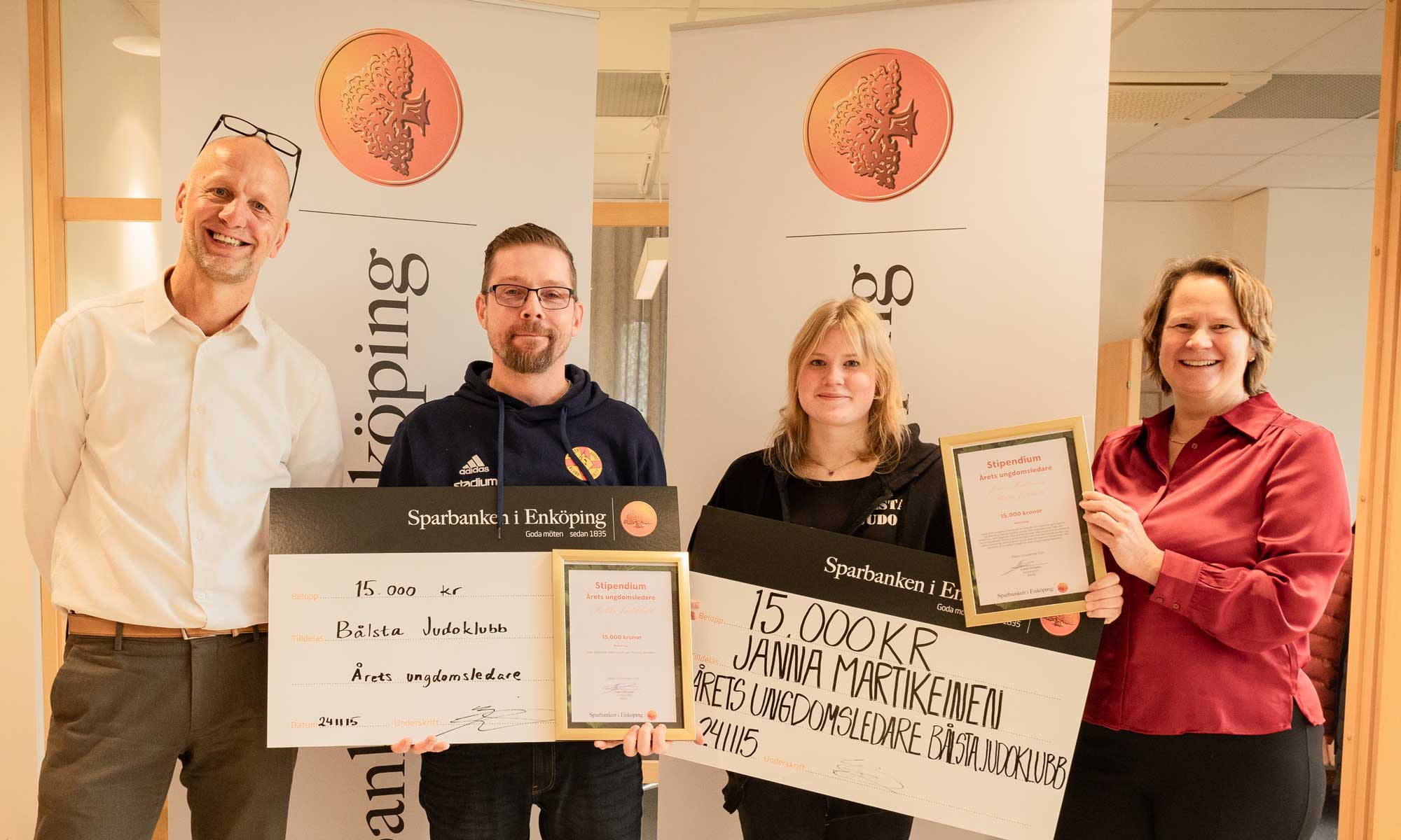 four people two of them dressed in black are holding big checks