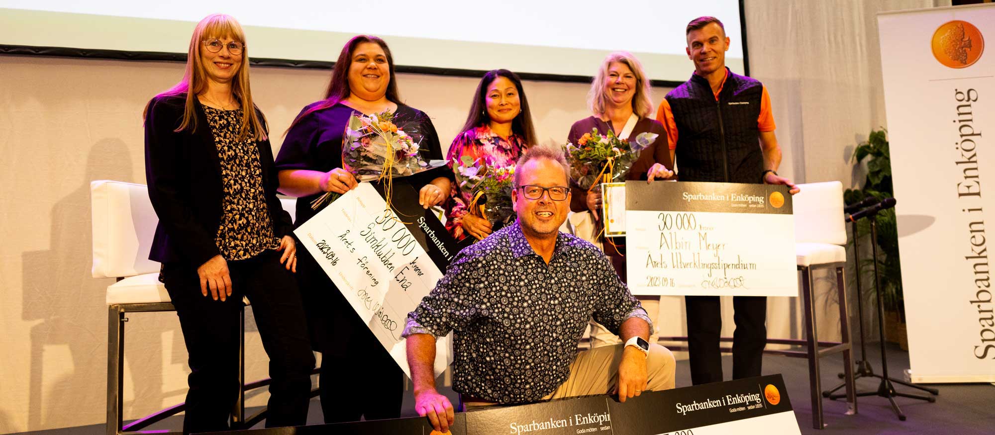 en grupp personer ler och håller diplom och blomsterbuketter